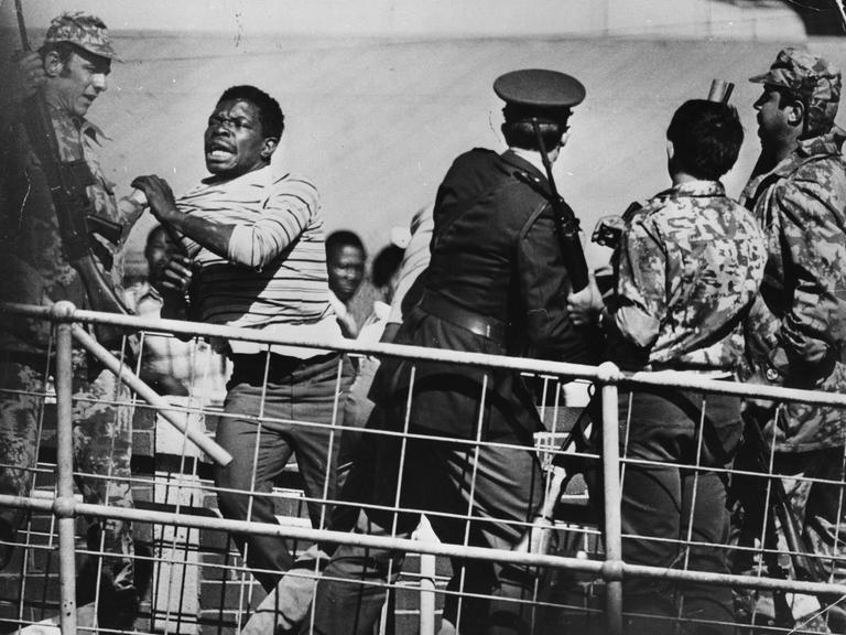 Während eines Anti-Apartheid Protests im Soweto Township in Südafrika rennt einer der Protestierenden in Richtung einer Absperrung während Polizisten und Soldaten versuchen, ihn aufzuhalten.