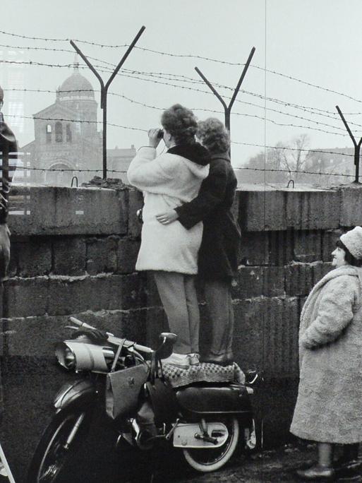 Das Foto zeigt den Versuch der Kontaktaufnahme auf der Westberliner Seite der Mauer am Leuschnerdamm (1963). Menschen stehen an der Mauer und gucken auf die andere Seite. Das Foto zeigt den Versuch der Kontaktaufnahme auf der Westberliner Seite der Mauer am Leuschnerdamm (1963). Menschen stehen an der Mauer und gucken auf die andere Seite.