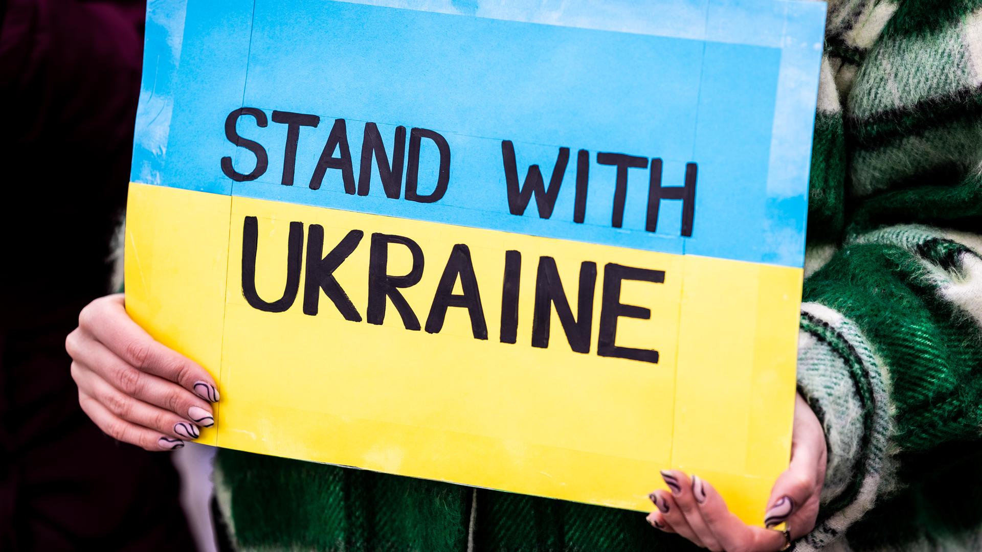 Der Schriftzug "Stand with Ukraine" ist auf dem Plakat einer Demonstrantin zu lesen.