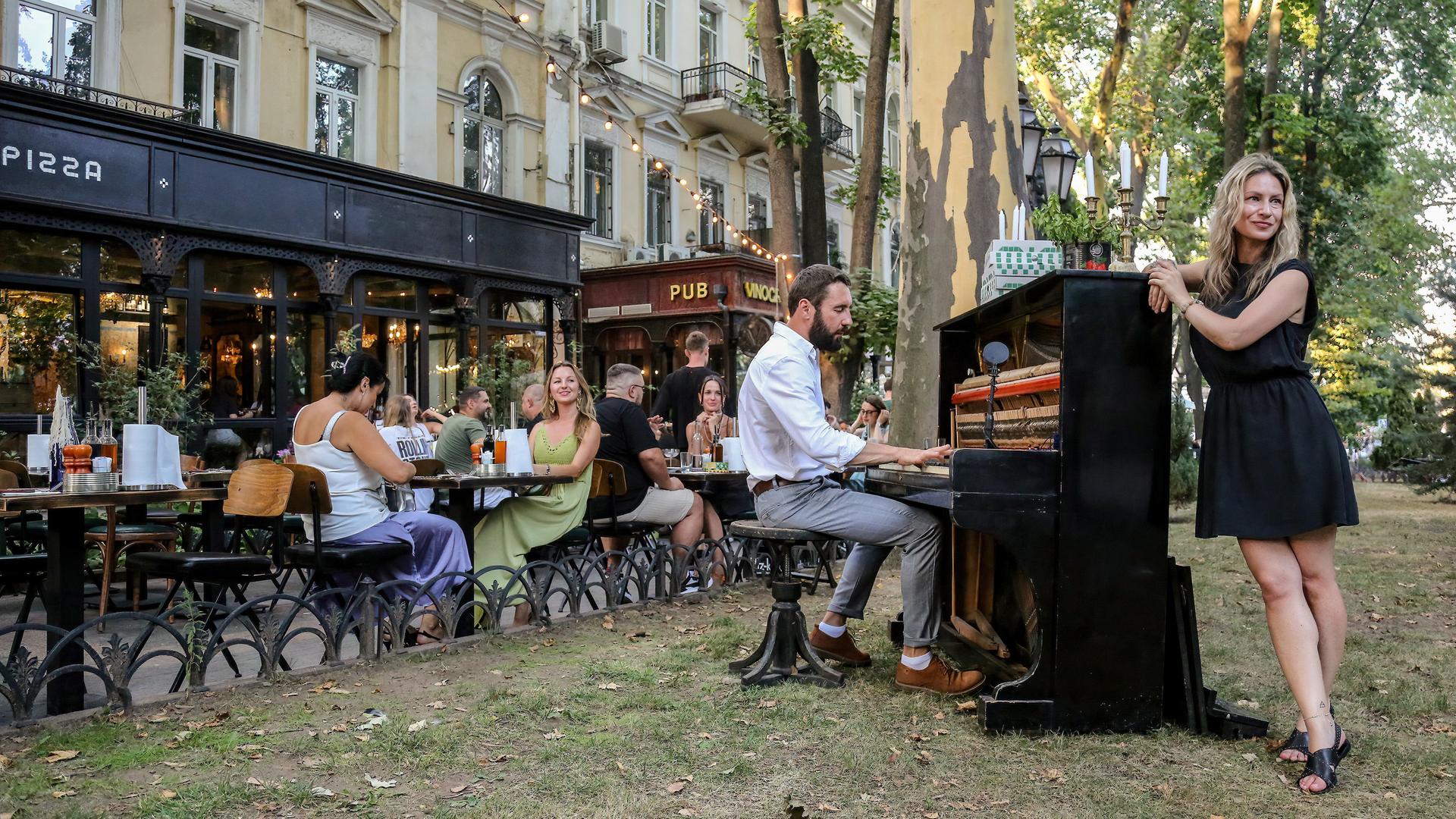 Straßenmusiker singen vor einem mit jungen Leuten besetzten Café in Odessa.