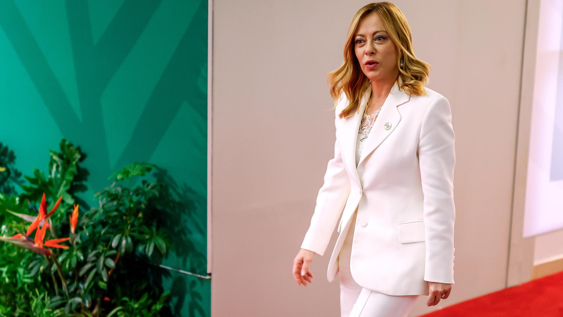 Italiens Regierungschefin Georgia Meloni läuft in einem weißen Hosenanzug einen Gang entlang. 