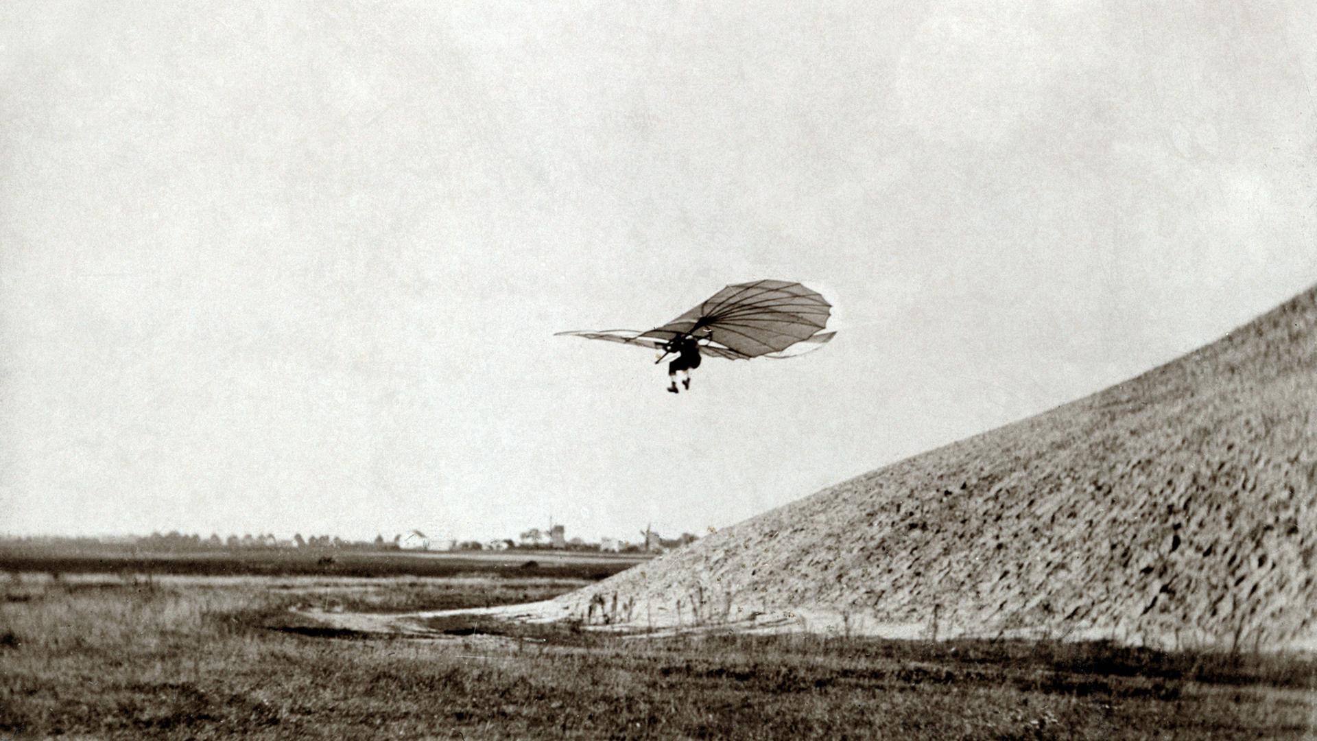 Flugpionier Otto Lilienthal fliegt mit einem Gleitflieger im 19. Jahrhundert von einem Hügel herunter.