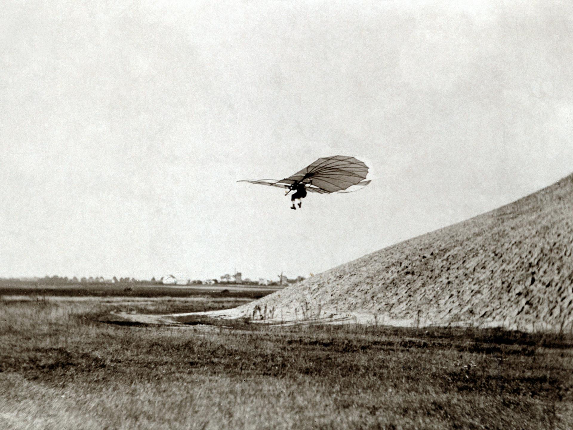 Flugpionier Otto Lilienthal fliegt mit einem Gleitflieger im 19. Jahrhundert von einem Hügel herunter.