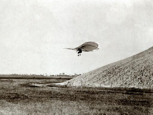 Flugpionier Otto Lilienthal fliegt mit einem Gleitflieger im 19. Jahrhundert von einem Hügel herunter.