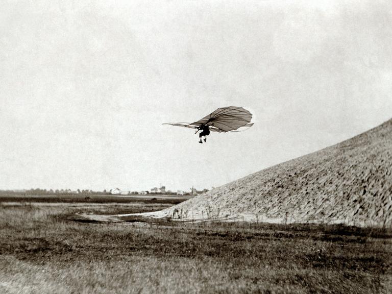 Flugpionier Otto Lilienthal fliegt mit einem Gleitflieger im 19. Jahrhundert von einem Hügel herunter.