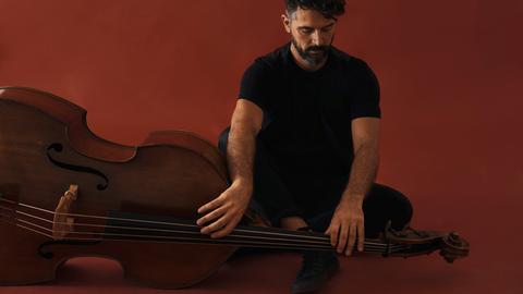 Petros Klampanis sitzt in einem rotroten Raum neben seinem Kontrabass.