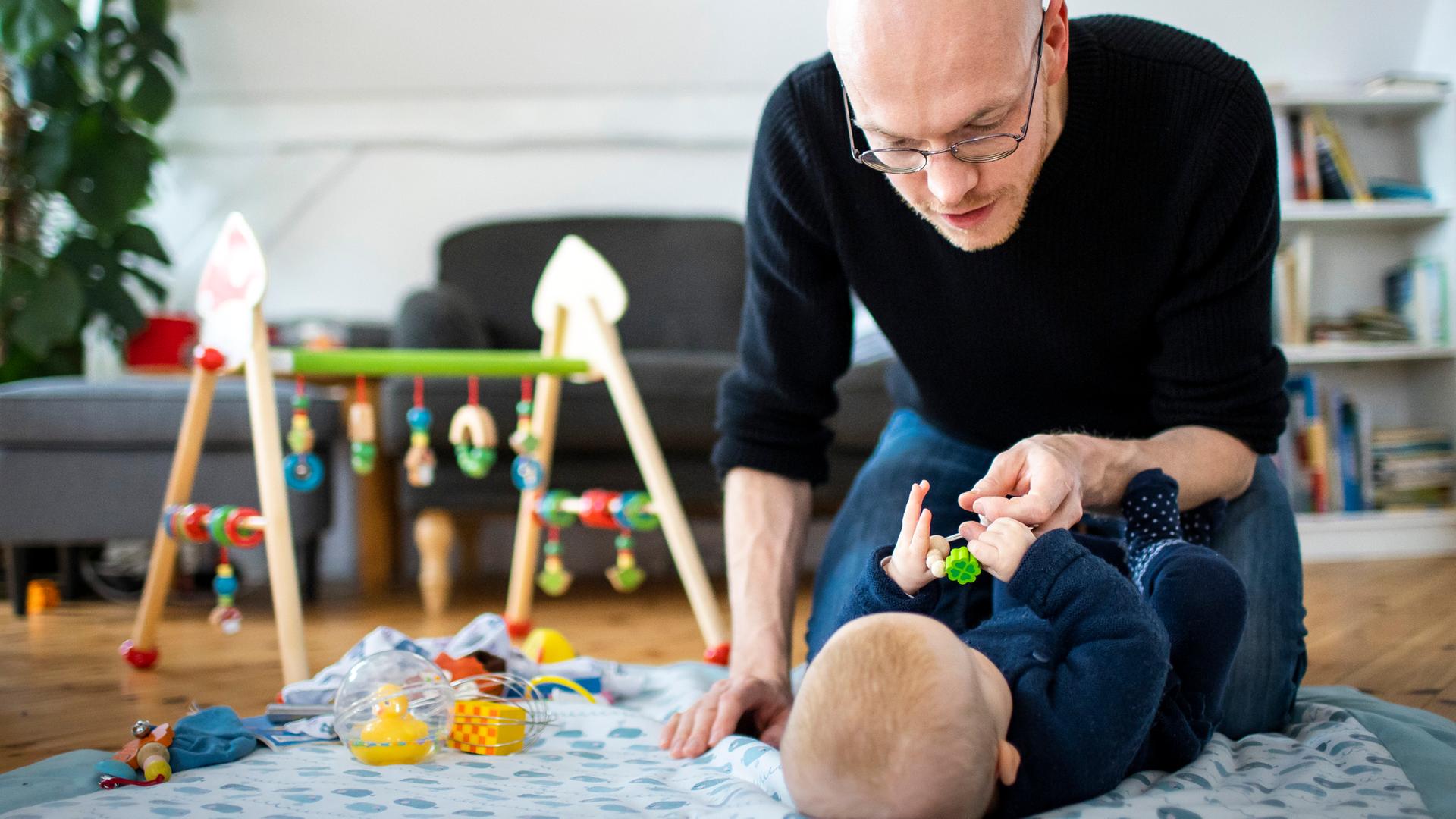 Ein Vater spielt mit seinem Baby auf einer Krabbeldecke.