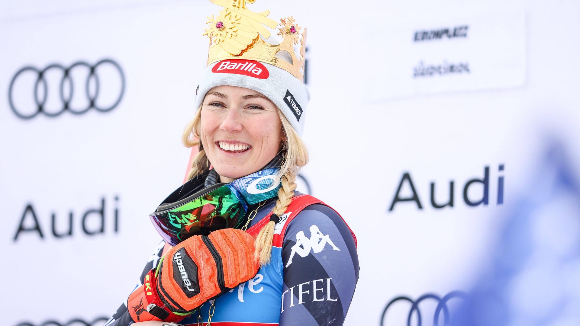 Mikaela Shiffrin in Skimontur lächelt nach einem Rennen vor einer weißen Werbenwand mit "Audi"-Schriftzügen.