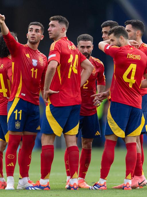 Zu sehen sind sieben spanische Spieler, die in einer Gruppe auf dem Feld stehen und sich besprechen.