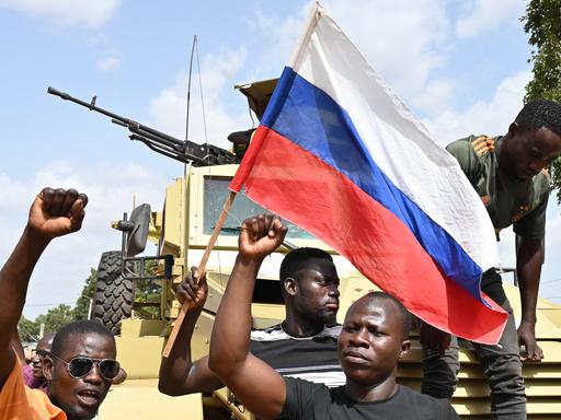 Eine Gruppe Demonstranten stehen vor einem Panzer und schwenken eine russische Flagge.