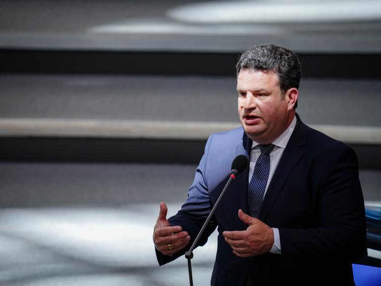 Ein Mann im einem dunkeln Anzug steht im Bundestag und hält eine Rede. Vor ihm ist ein Mikrofon. Das Licht bricht sich vor im, so dass er im Halbdunklen steht. Es ist der SPD-Politiker und Arbeitsminister Hubertus Heil.