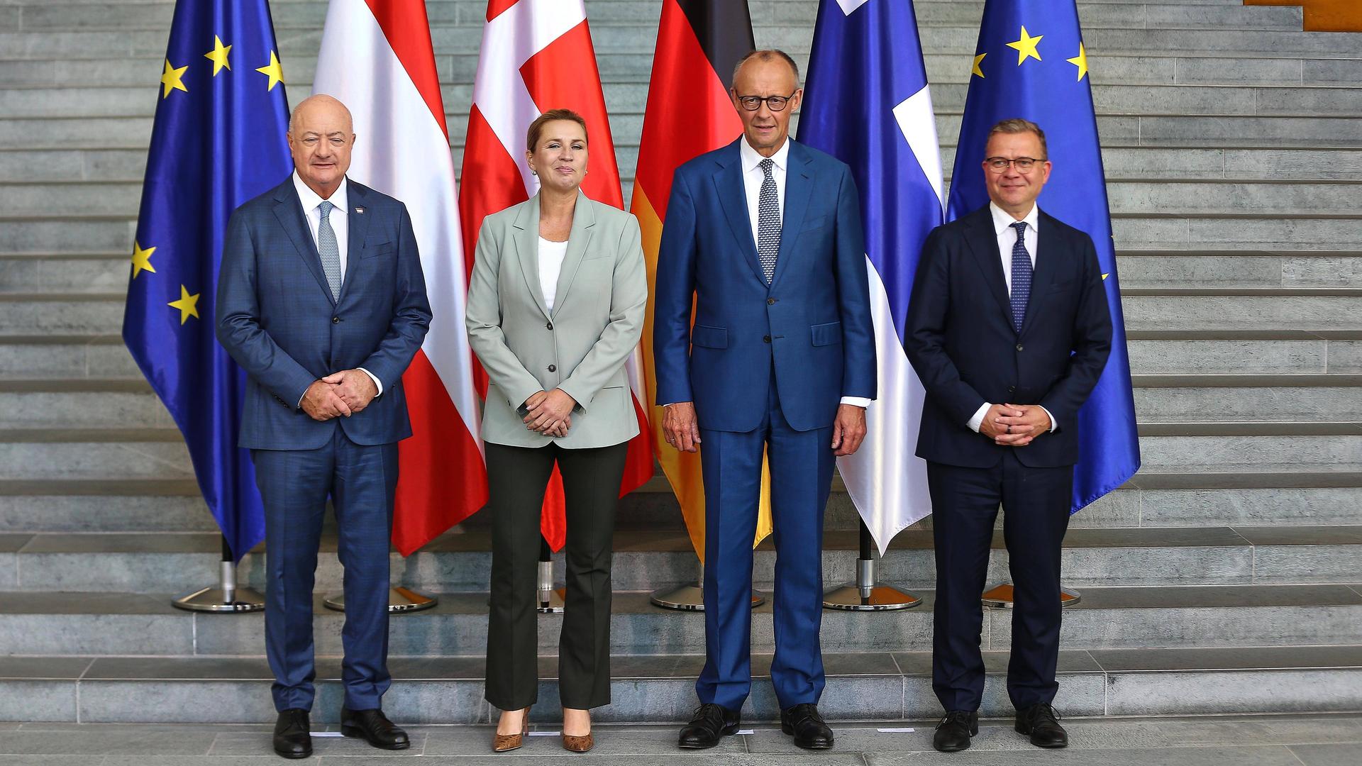 Die Regierungschefs Christian Stocker (Österreich), Mette Frederiksen (Dänemark), Friedrich Merz und Petteri Orpo (Finnland) posieren für ein Gruppenfoto vor ihren jeweiligen Landesflaggen.