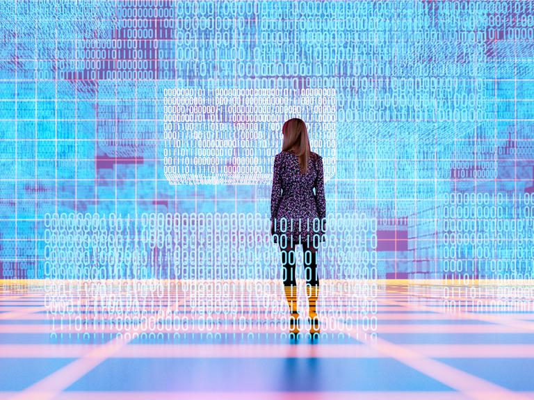 Eine weibliche Persons steht in einem digitalen Raum und schaut auf zahlreiche Coding-Reihen