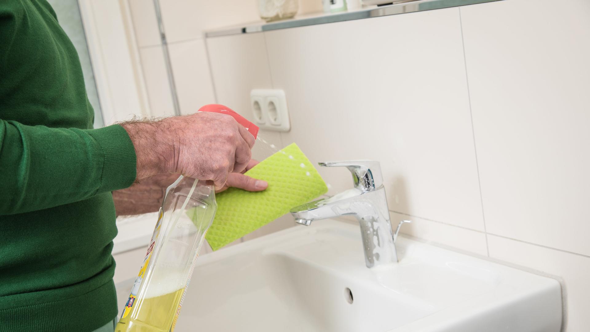 Ein Mann putzt ein Waschbecken mithilfe eines Lappens und Putzmittel.