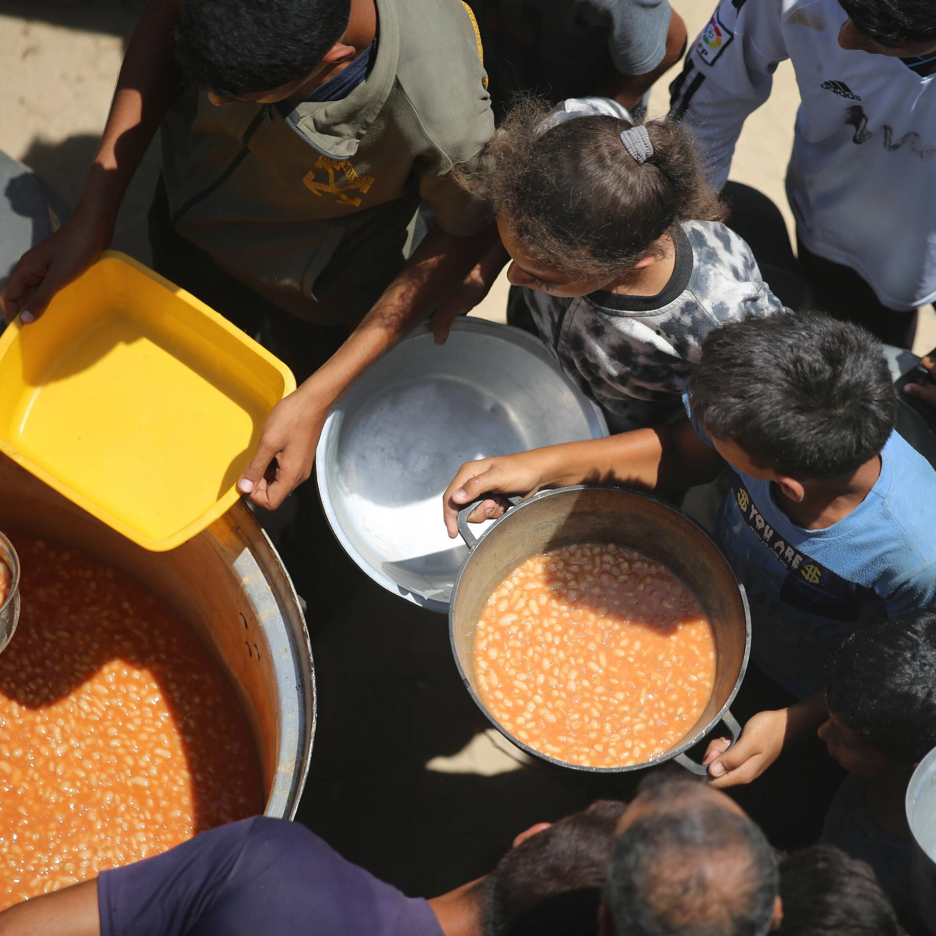 Im Gazastreifen wird aus großen Töpfen Essen an Kinder verteilt.
