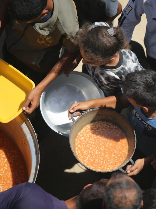 Im Gazastreifen wird aus großen Töpfen Essen an Kinder verteilt.
