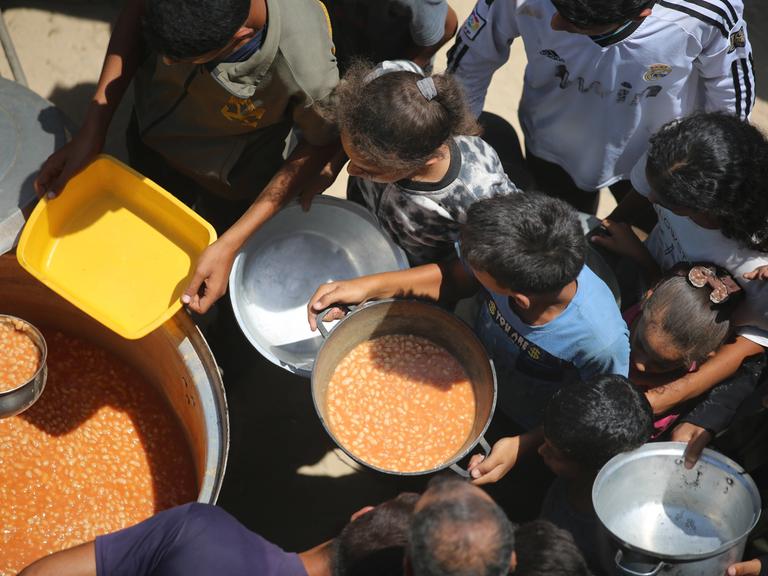 Im Gazastreifen wird aus großen Töpfen Essen an Kinder verteilt.