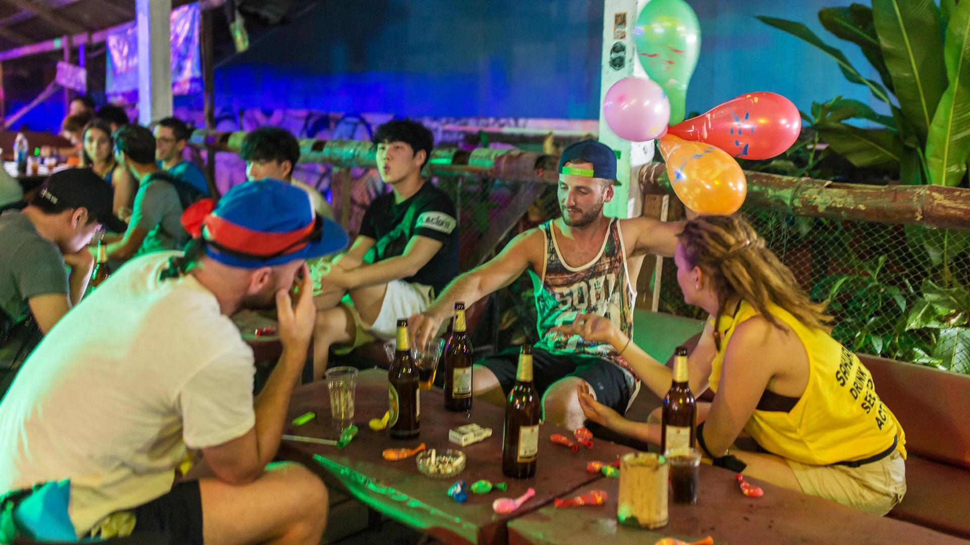 Die Stadt Vang Vieng in Laos: Junge Menschen sitzen an einem Tisch und trinken Alkohol.