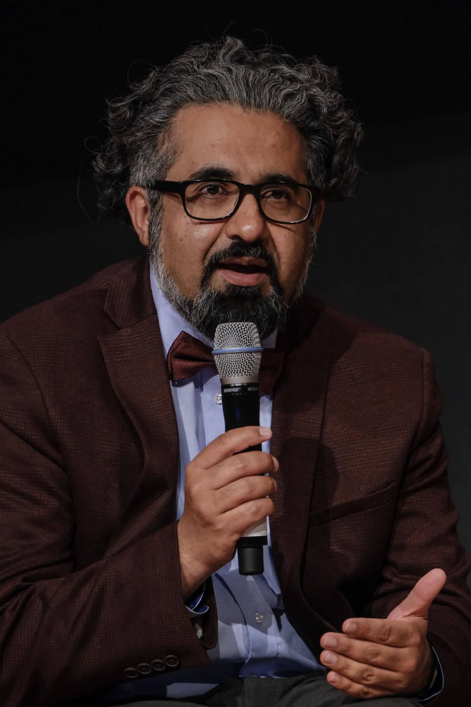 Der Islamwissenschaftler Ahmad Milad Karimi trägt ein rotbraunes Sakko und eine gleichfarbige Fliege und spricht in ein Mikrofon, das er in der rechten Hand hält.