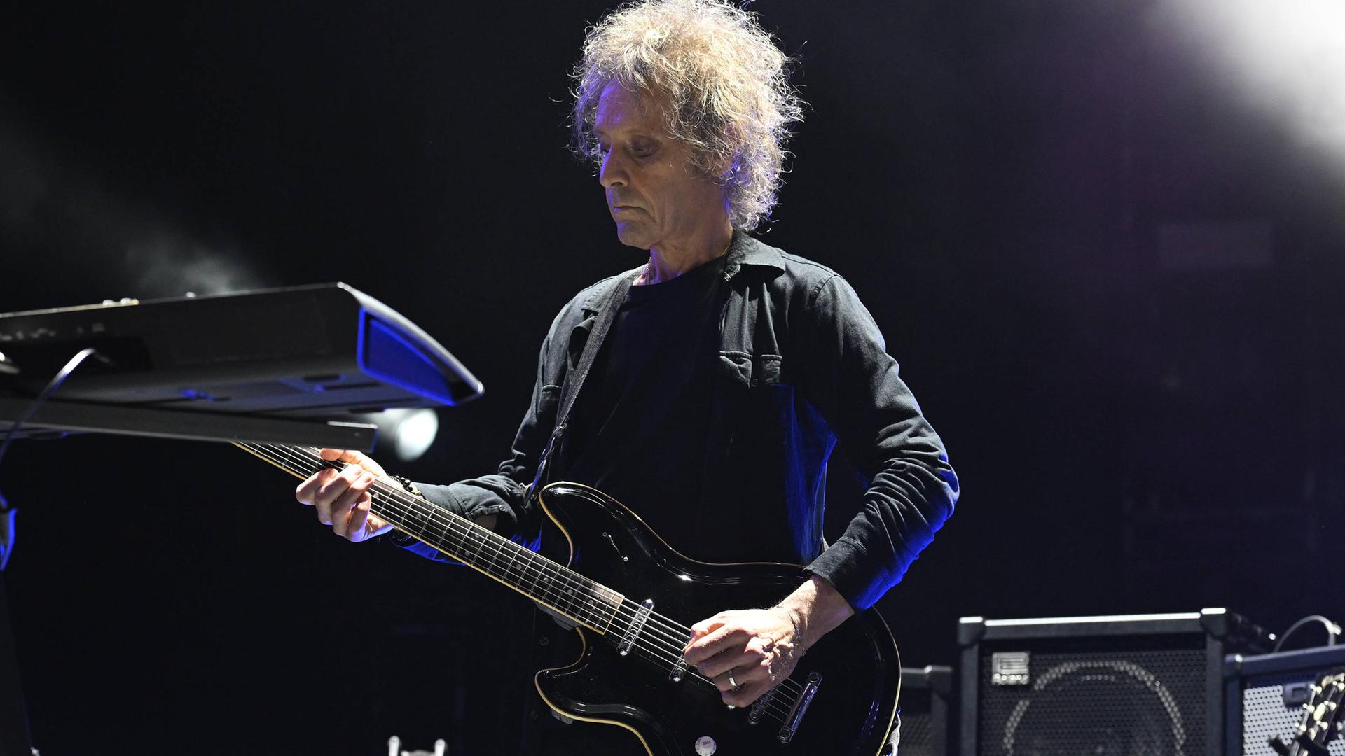 Der Musiker Perry Bamonte spielt mit ernster Miene und konzentriert wirkend bei einem Konzert auf seiner Gitarre. 