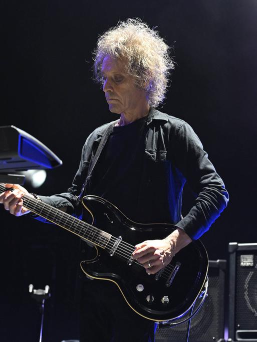 Der Musiker Perry Bamonte spielt mit ernster Miene und konzentriert wirkend bei einem Konzert auf seiner Gitarre. 