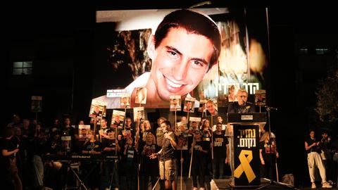 Es ist dunkel. Das lächelnde Gesicht Hard Goldins ist auf einer großen Leinwand zu sehen. Davor viele Demonstranten mit Plakaten, auf denen andere Geiseln abgebildet sind. 