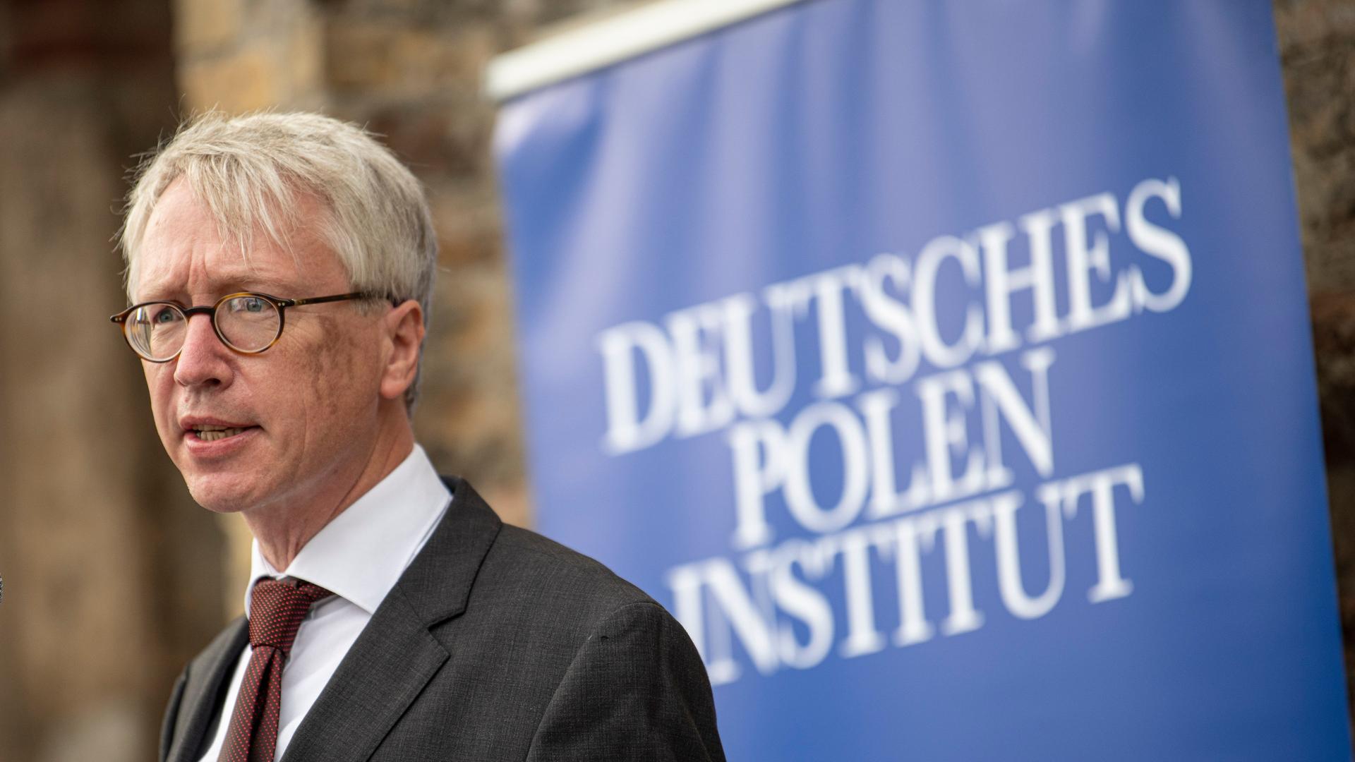 Peter Oliver Loew, Direktor des Deutschen Polen Instituts, vor einem blauen Banner mit der Aufschrift seines Instituts. 