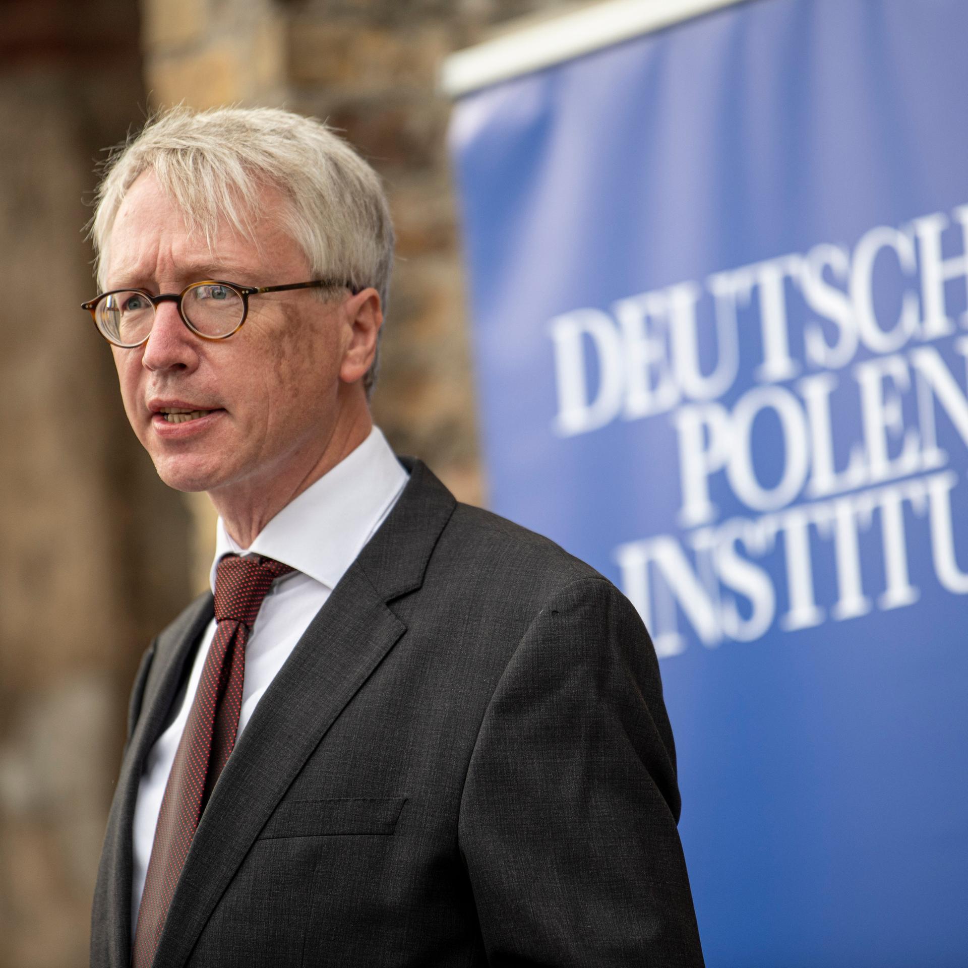 Peter Oliver Loew, Direktor des Deutschen Polen Instituts, vor einem blauen Banner mit der Aufschrift seines Instituts. 