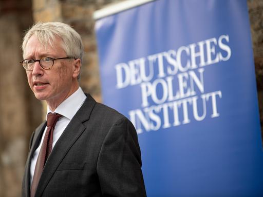 Peter Oliver Loew, Direktor des Deutschen Polen Instituts, vor einem blauen Banner mit der Aufschrift seines Instituts. 