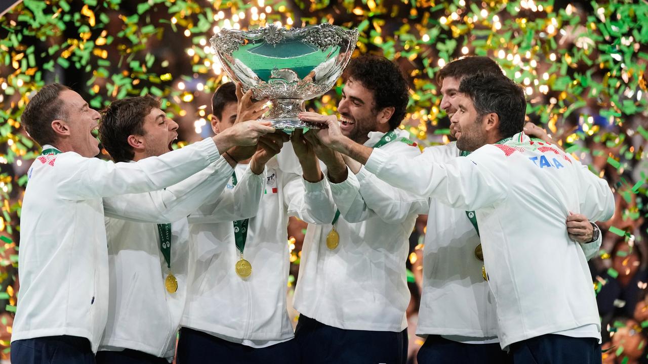 Mehrere Sportler in weißen Jacken halten zusammen eine Trophäe hoch.