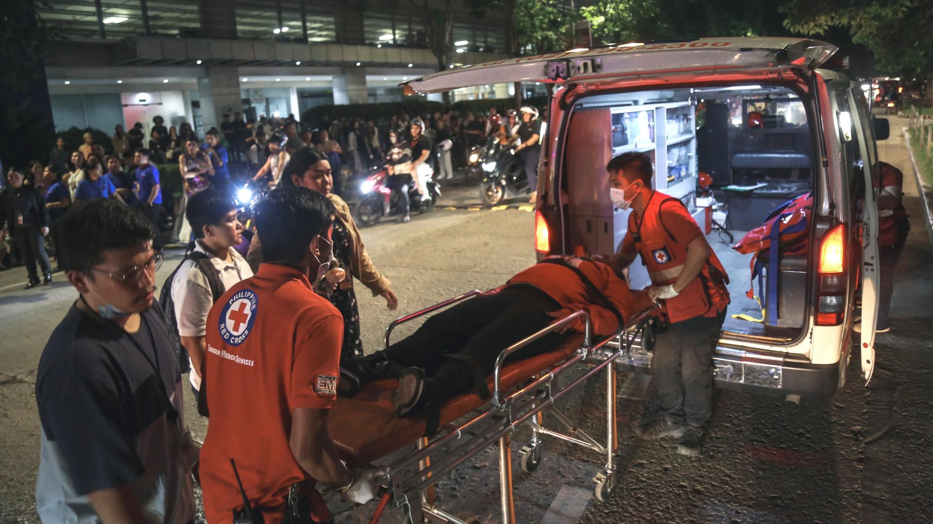 Sanitäter heben einen Geretteten auf einer Bahre in einen Krankenwagen. Im Hintergrund sind Anwohner zu sehen, die sich ins Freie begeben haben.