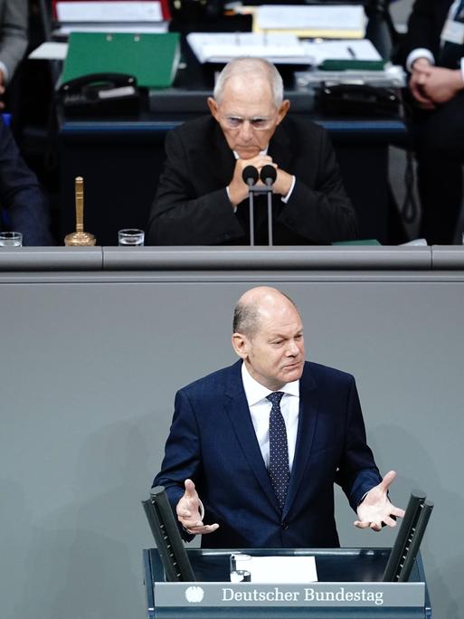 Bundeskanzler Scholz gestikuliert hinter einem Rednerpult. Über ihm thront Bundestagspräsident Schäuble. 