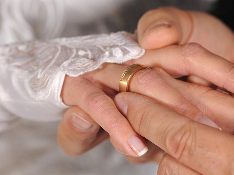 Nahaufnahme von Händen: Bräutigam steckt der Braut den Ring an.