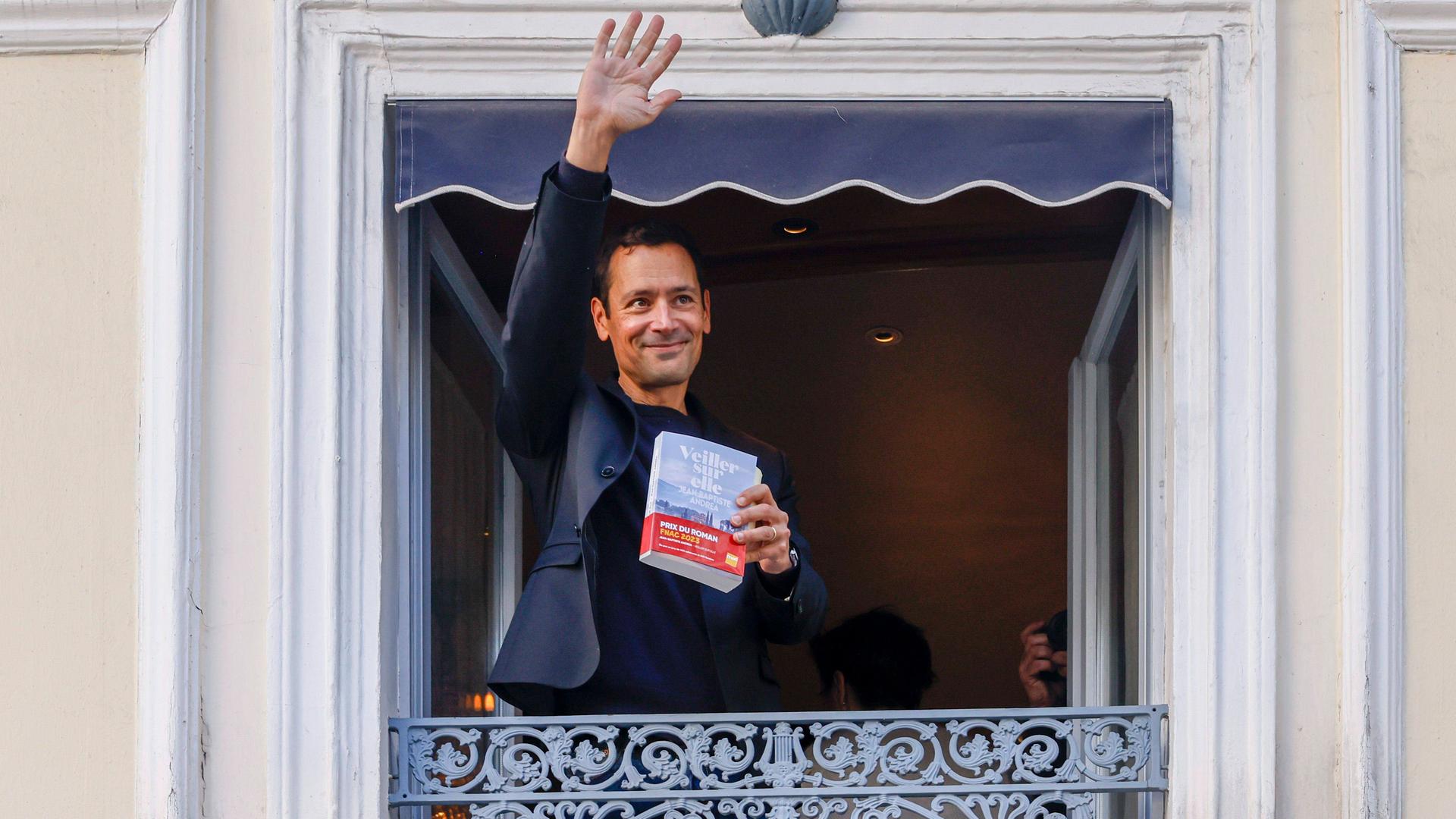 Autor Jean-Baptiste Andrea winkt nach dem Gewinn des Prix Goncourt im November 2023 mit seinem Roman "Veiller sur elle" in der Hand von einem Balkon aus. Autor Jean-Baptiste Andrea winkt nach dem Gewinn des Prix Goncourt im November 2023 mit seinem Roman "Veiller sur elle" in der Hand von einem Balkon aus.