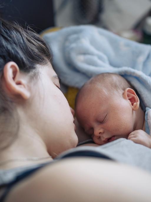 Nahaufnahme eines neugeborenen Babys, das mit geschlossenen Augen auf der Brust der Mutter liegt.