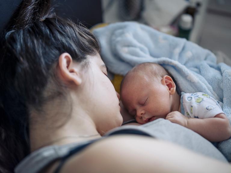 Nahaufnahme eines neugeborenen Babys, das mit geschlossenen Augen auf der Brust der Mutter liegt.
