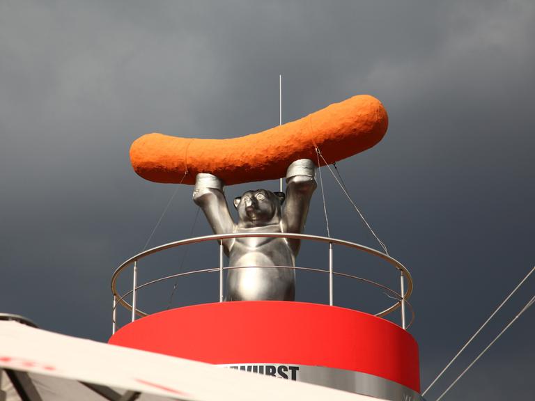 Skulptur eines Bären mit Wurst auf einem Imbiss in Berlin, vor wolkenverhangenem Himmel