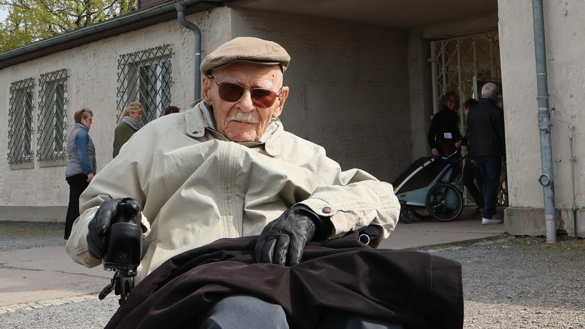 Raymond Renaud aus Frankreich sitzt im Rollstuhl vor einem Tor des ehemaligen NS-Konzentrationslagers Buchenwald.