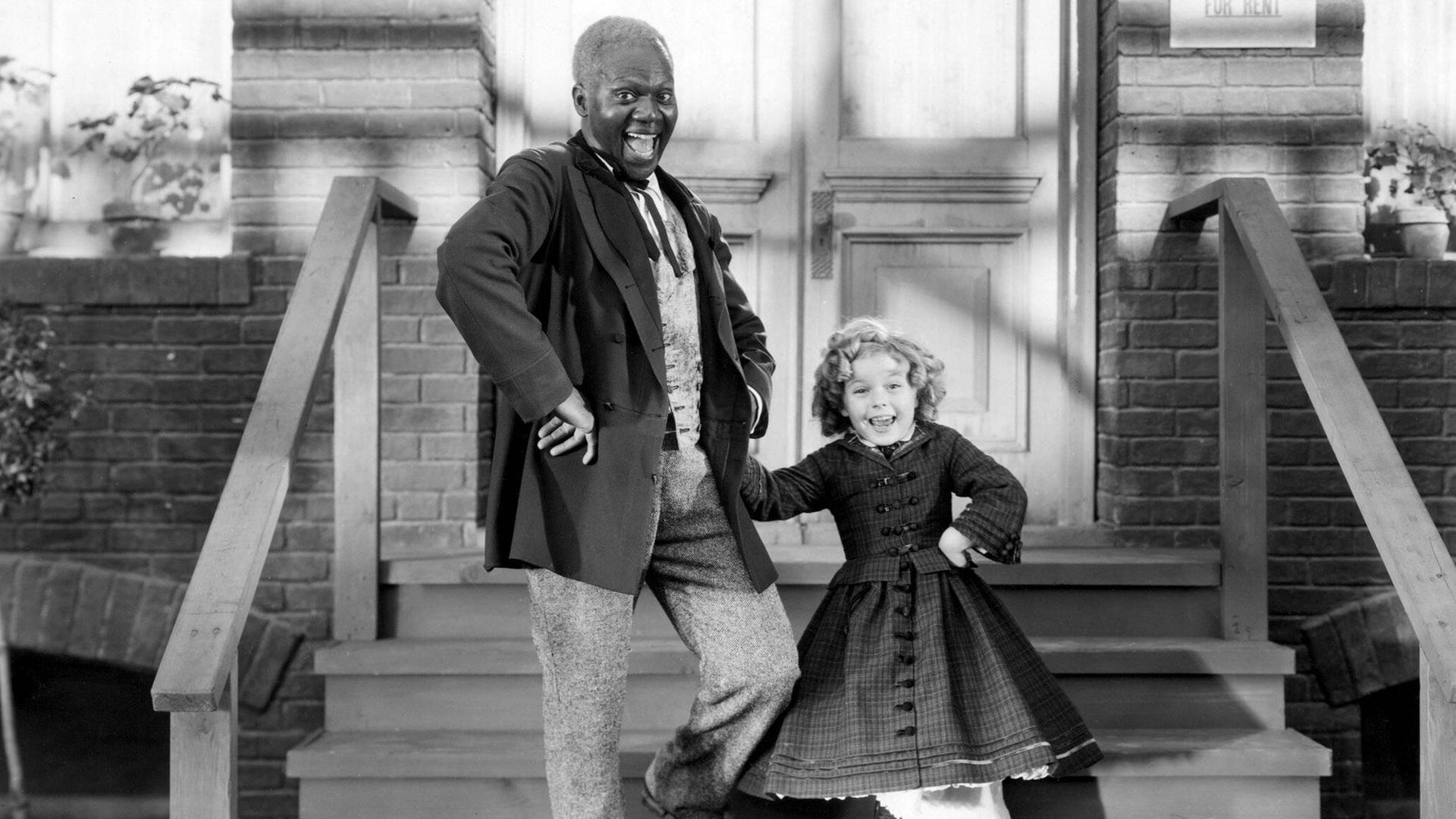 Bill Robinson und Shirley Temple stehen auf einer Treppe vor einem Haus