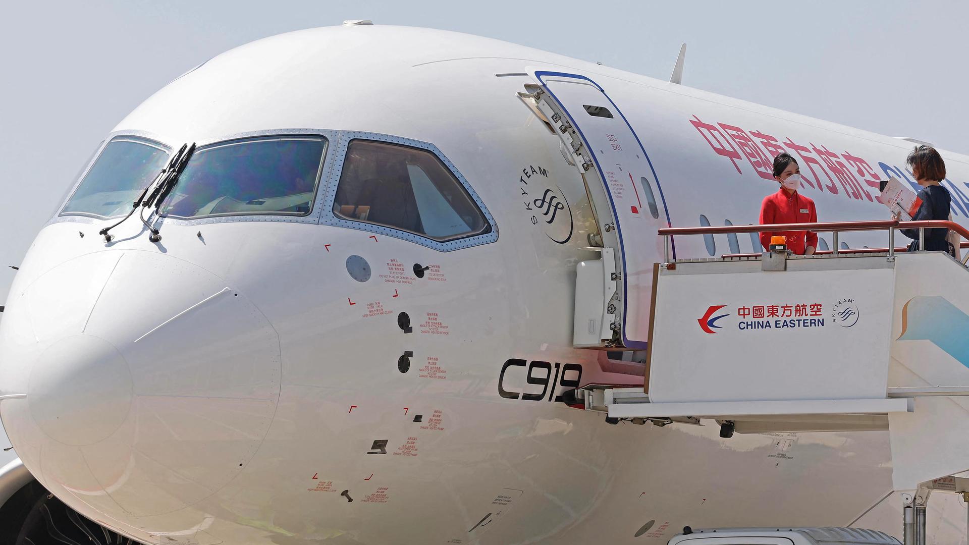 Ein chinesische Passagiermaschine steht auf dem Flughafen in Shanghai, rechts im Bild eine in rot gekleidete Stewardess mit Mundschutz. Ein chinesische Passagiermaschine steht auf dem Flughafen in Shanghai, rechts im Bild eine in rot gekleidete Stewardess mit Mundschutz.