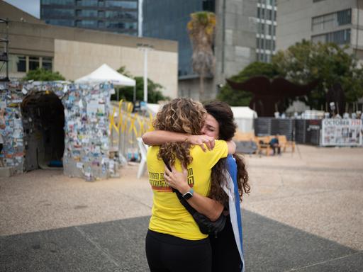 Zwei Frauen umarmen sich auf dem Platz der Geiseln in Tel Aviv. Die eine hat eine israelische Flagge umgebunden, die andere trägt ein gelbes T-Shirt, das die Forderung nach Freilassung der Geiseln symbolisiert.