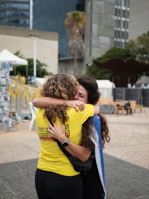 Zwei Frauen umarmen sich auf dem Platz der Geiseln in Tel Aviv. Die eine hat eine israelische Flagge umgebunden, die andere trägt ein gelbes T-Shirt, das die Forderung nach Freilassung der Geiseln symbolisiert.