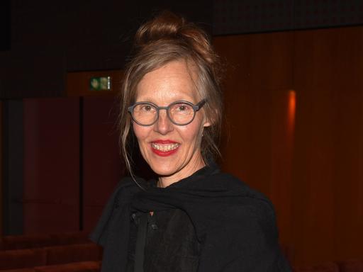 Porträt von Donata Wenders vor dunklem Hintergrund. Sie lacht in die Kamera.