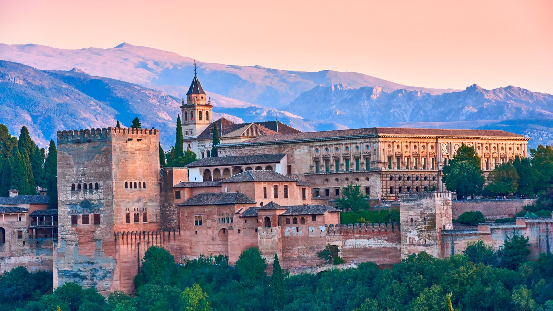 Eine burgähnliche riesige Palastanlage im Grünen vor dem Hintergrund von Bergen.