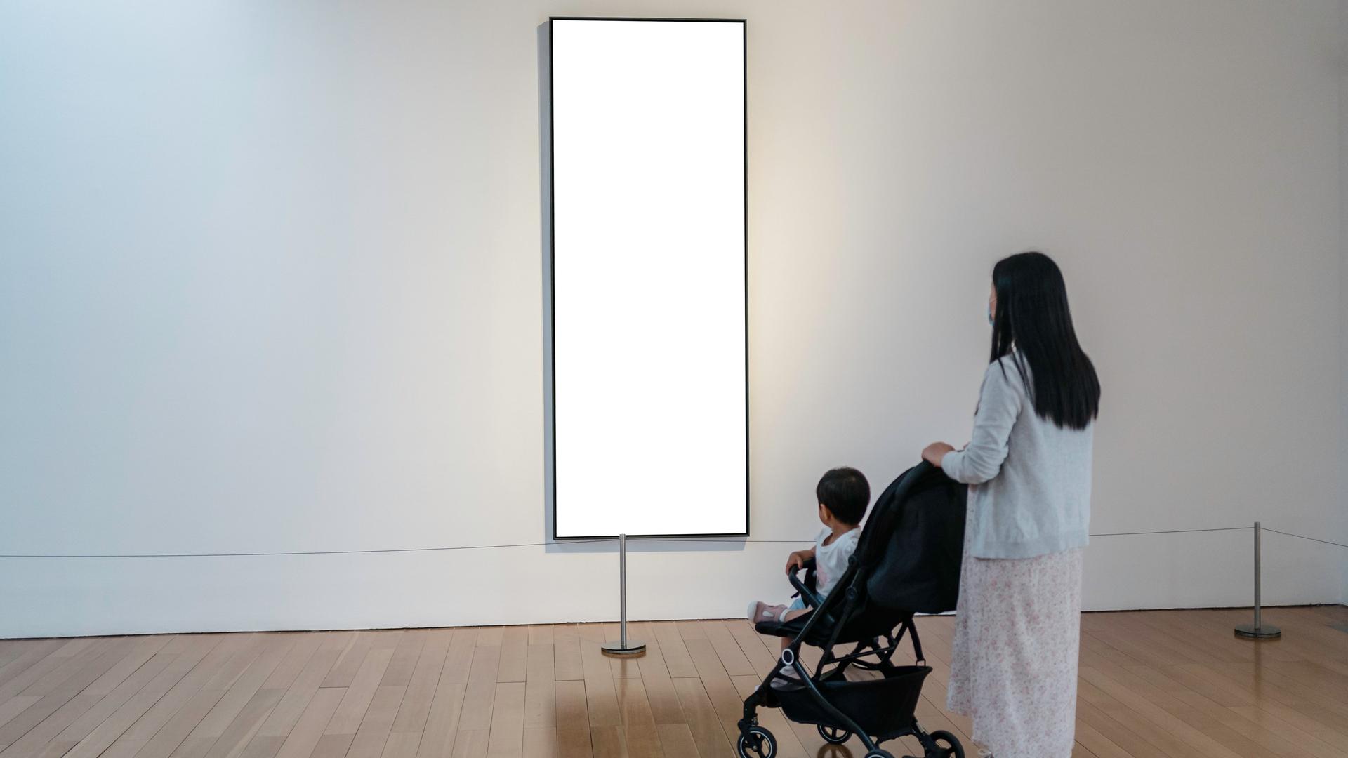 Eine Frau mit einem Kinderwagen in einer Galerie vor einem leeren weißen Bild. Eine Frau mit einem Kinderwagen in einer Galerie vor einem leeren weißen Bild.