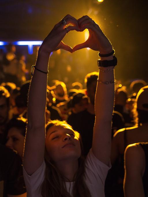 Zwei junge Hände bilden bei einem Konzert ein Herz über den Köpfen der Besucher eines Konzertes. 