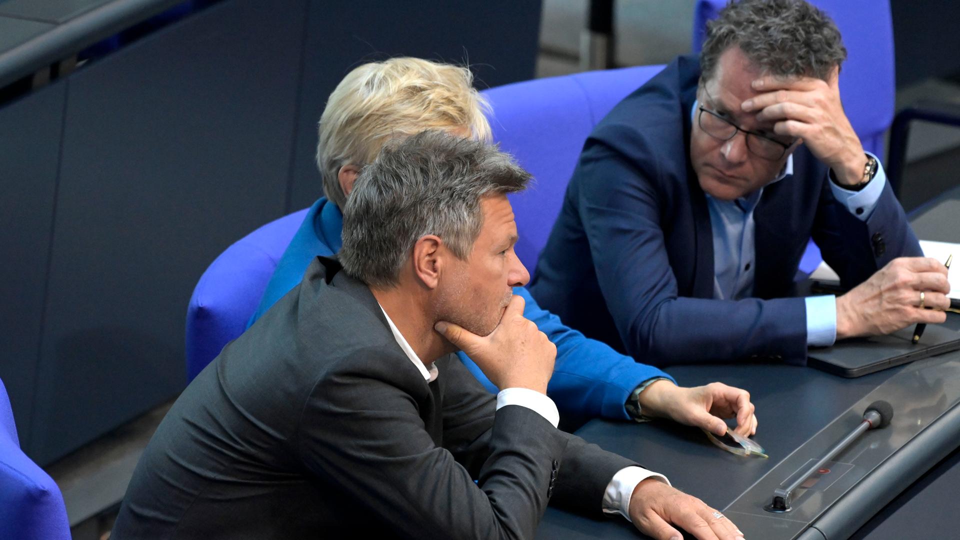 Robert Habeck, Renate Künast und Harald Ebner sitzen am 24. Mai 2023 im Bundestag und schauen einander an. Habeck und Ebner scheinen besorgt zu sein.