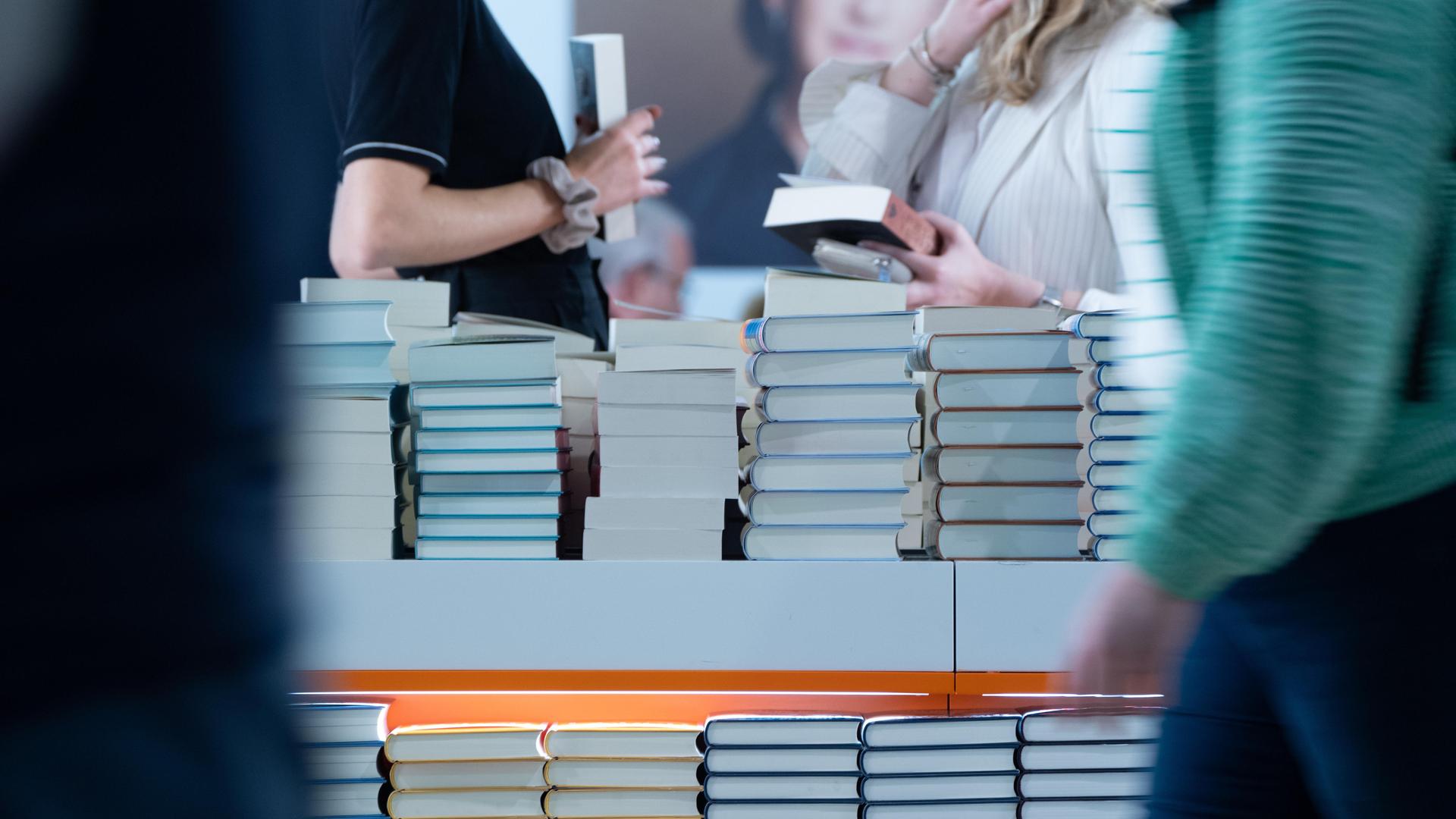 An einem Tisch auf dem sich Bücher stapeln, stehen Menschen, die Bücher in den Händen halten