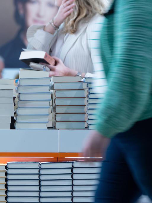 An einem Tisch auf dem sich Bücher stapeln, stehen Menschen, die Bücher in den Händen halten