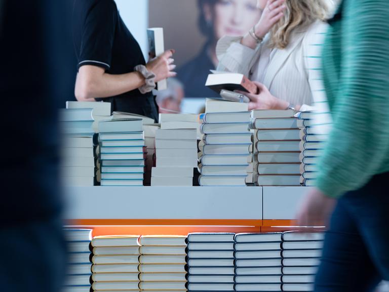 An einem Tisch auf dem sich Bücher stapeln, stehen Menschen, die Bücher in den Händen halten